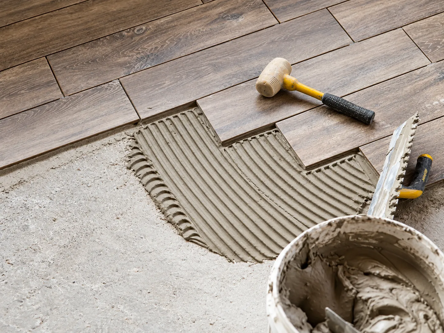 Floor tile being laid on adhesive with a mallet and trowel
